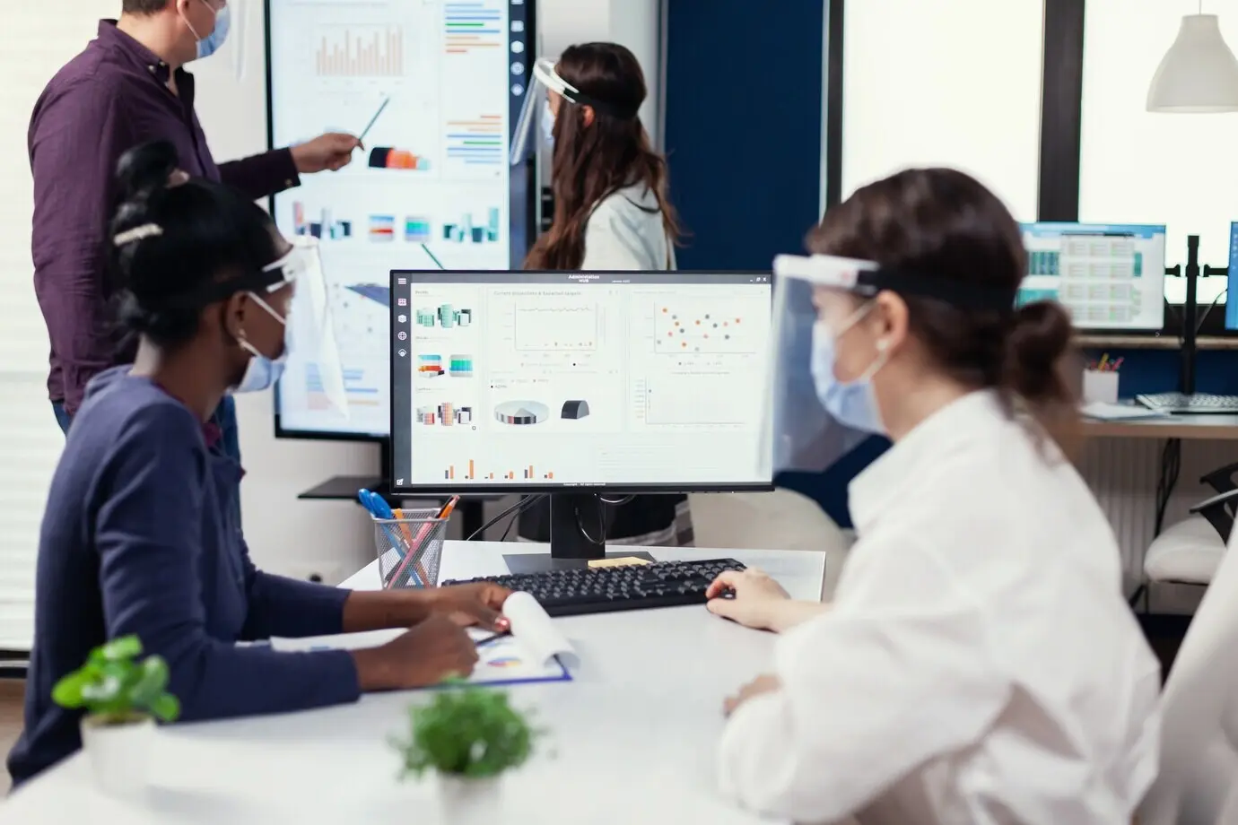 Сотрудник из Африки слушает тренера на конференции по продажам во время COVID-19. Многонациональная команда работает в компании в рамках новой нормы, соблюдая социальную дистанцию в период глобальной пандемии коронавируса.